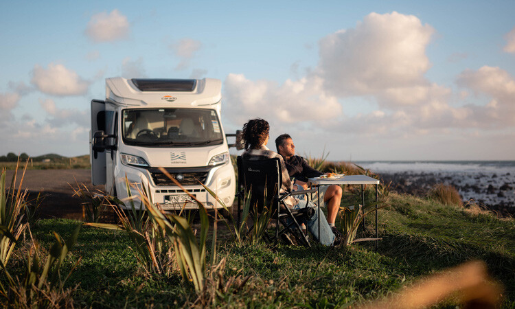 A couple relaxing outside of their Wilderness Motorhome on a summer evening