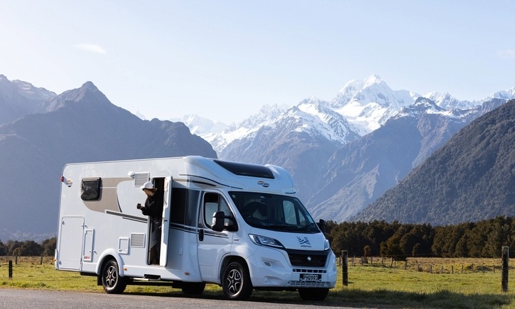 A woman looking out the view outside of her Wilderness motorhome rental in NZ while enjoying coffee