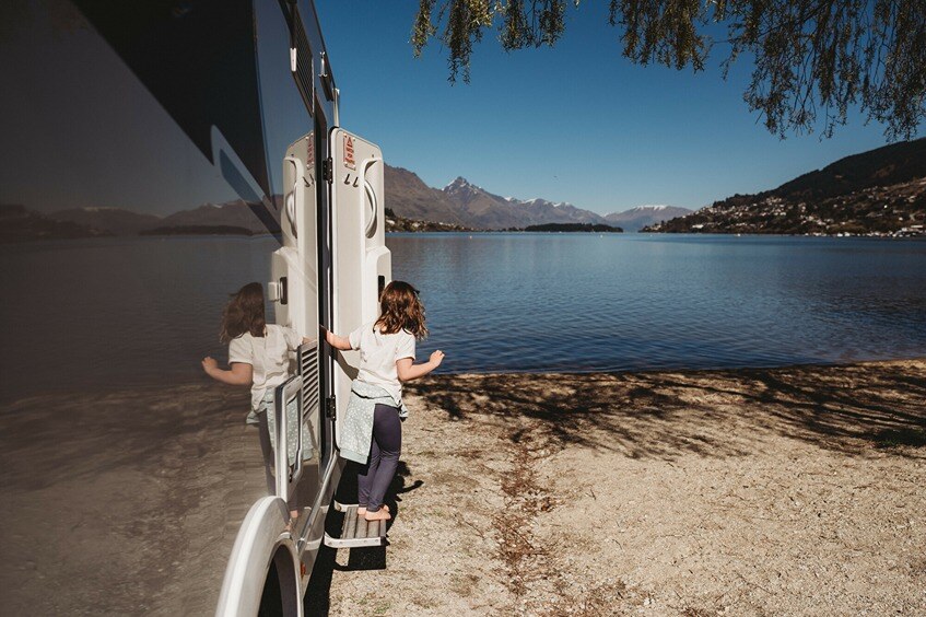 A kid hopping out of a motorhome to explore a front lake