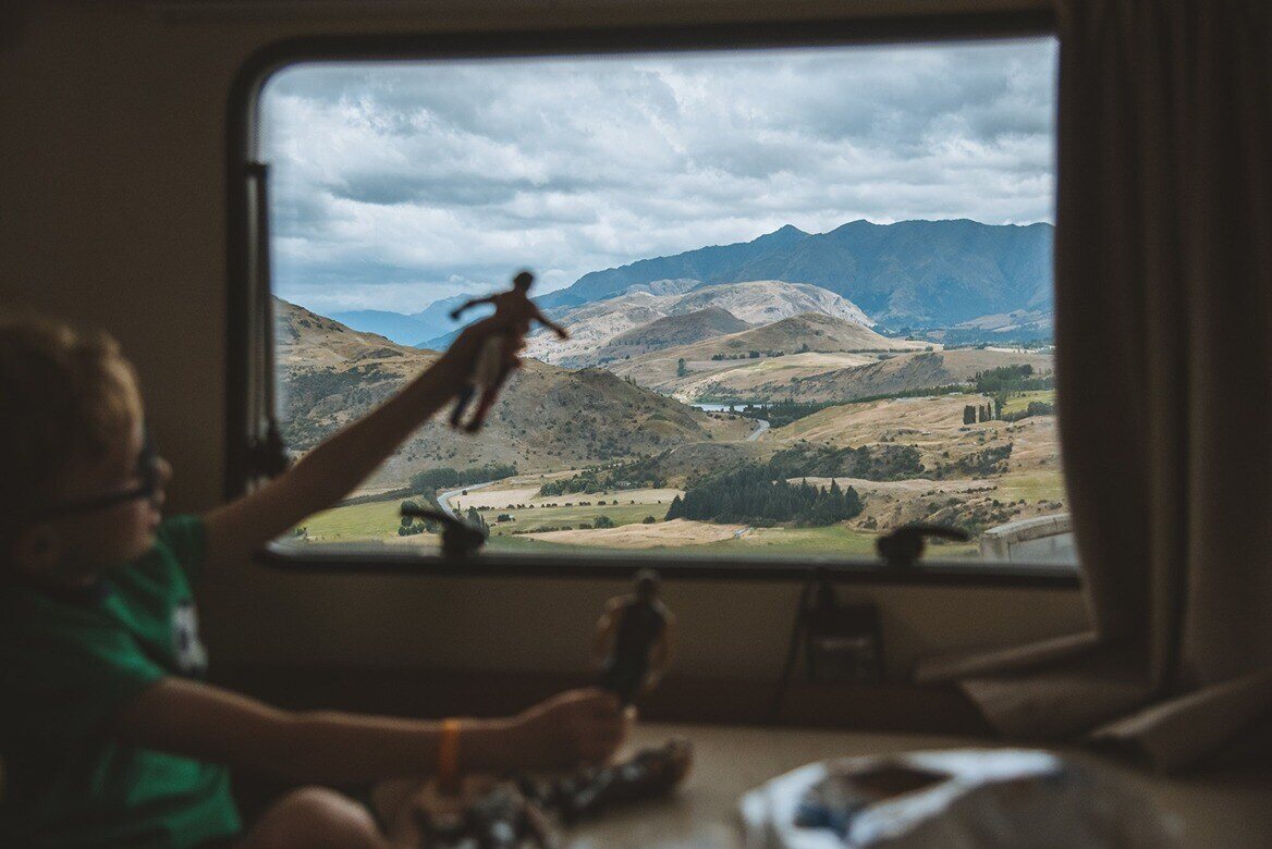 Kid playing a toy beside a motorhome window with hills in the backdrop