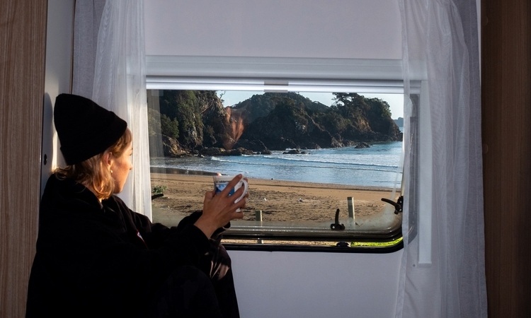 A woman enjoying her coffee inside a motorhome while looking at the view outside