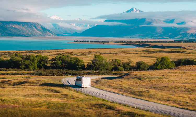 A Wilderness motorhome being driven on a road with beutiful lake and mountain landscape 